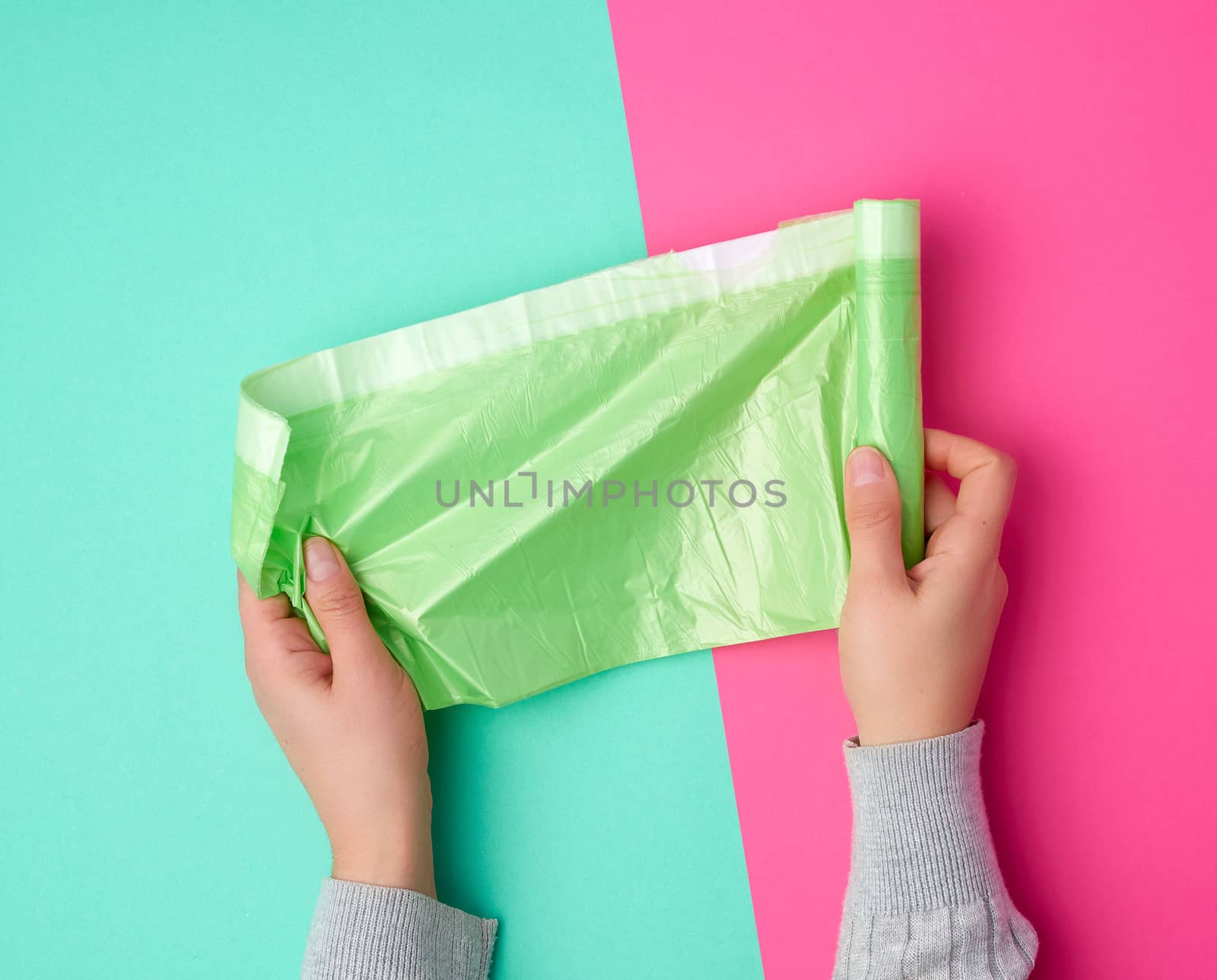 female hand unwinds a green plastic bag for rubbish, green pink background