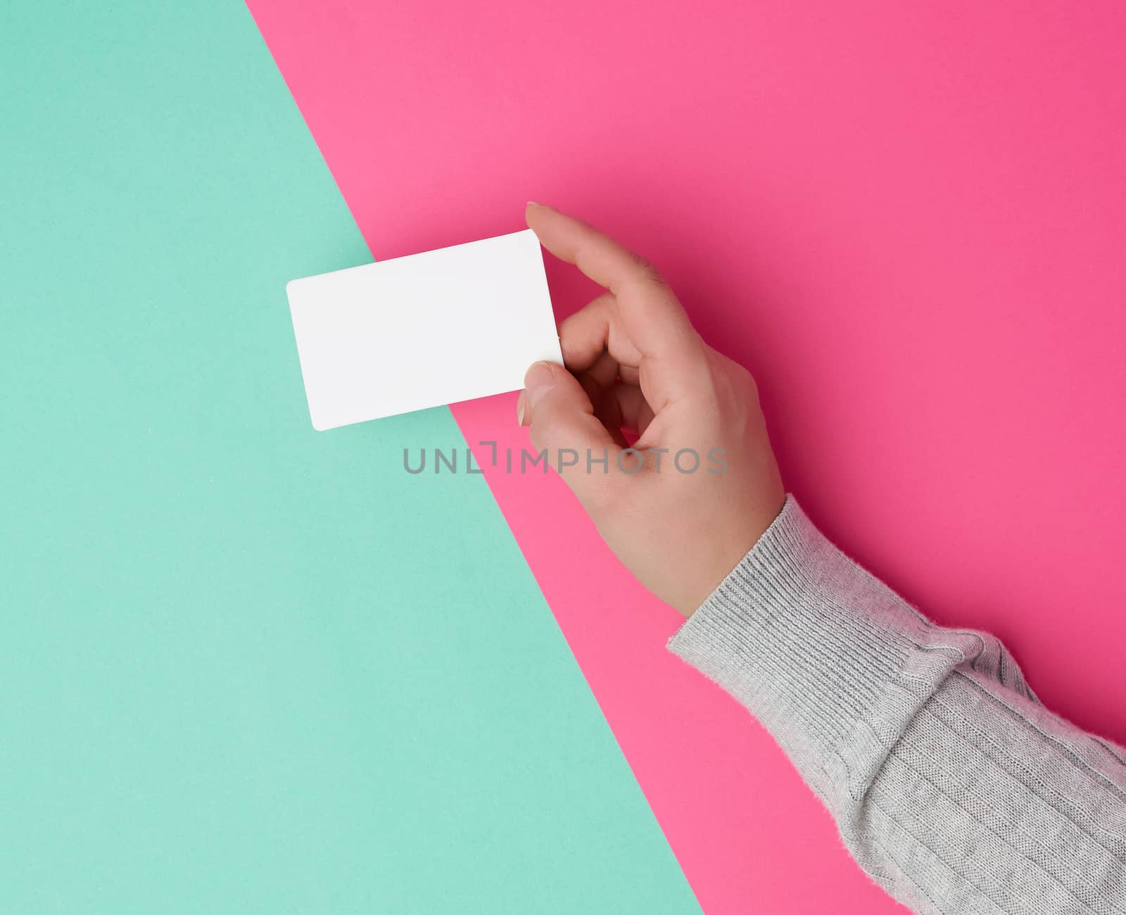 female hand holding empty white paper business card on a colored background, top view
