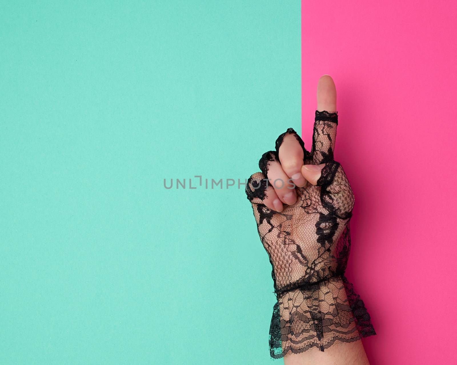 hand in a black lace glove on a pink-green background, top view, finger raised up