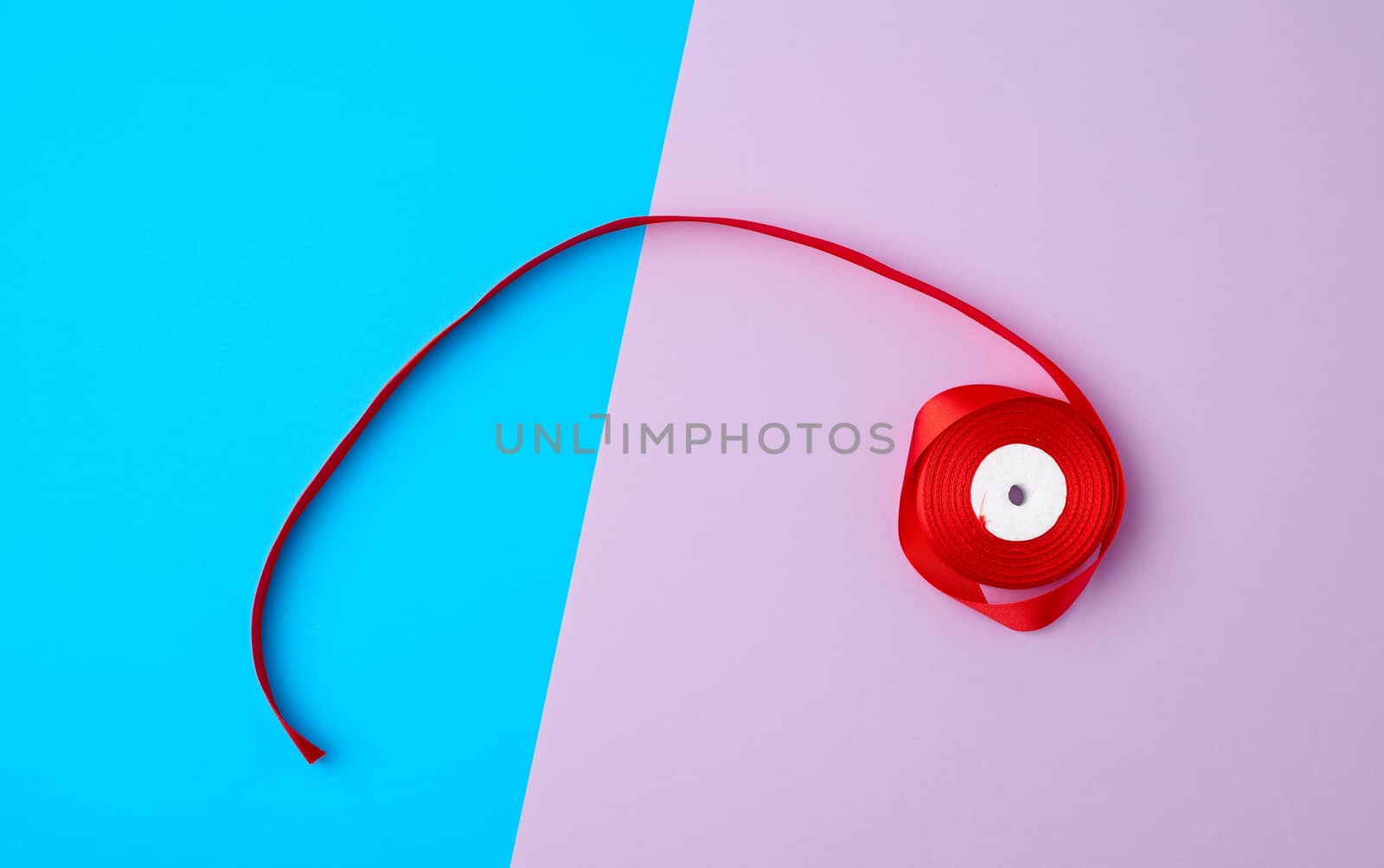 spools with red satin ribbon on a color background, top view
