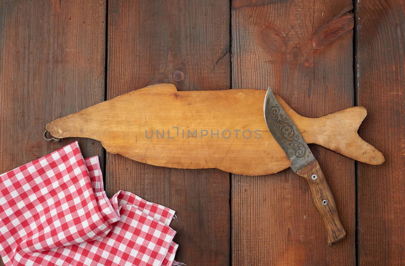 wooden cutting board in the shape of a fish and a sharp knife, brown table from boards, top view