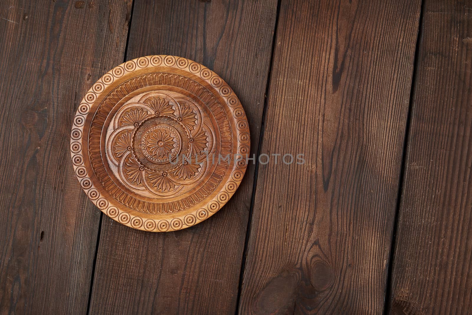 empty round brown carved decorative plate standing on a wooden background from old boards, top view