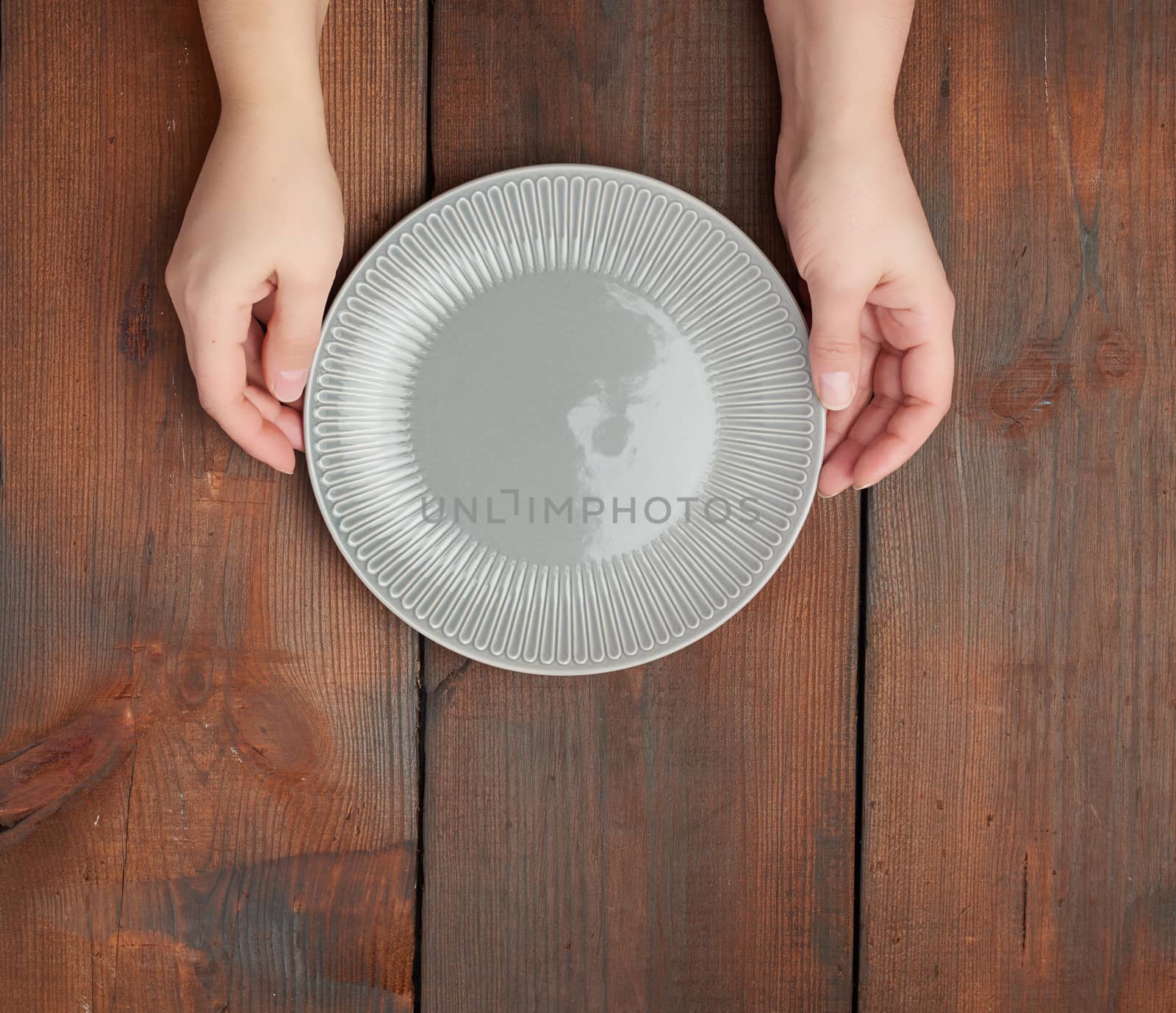 hands hold empty gray round ceramic plate, wooden background, top view