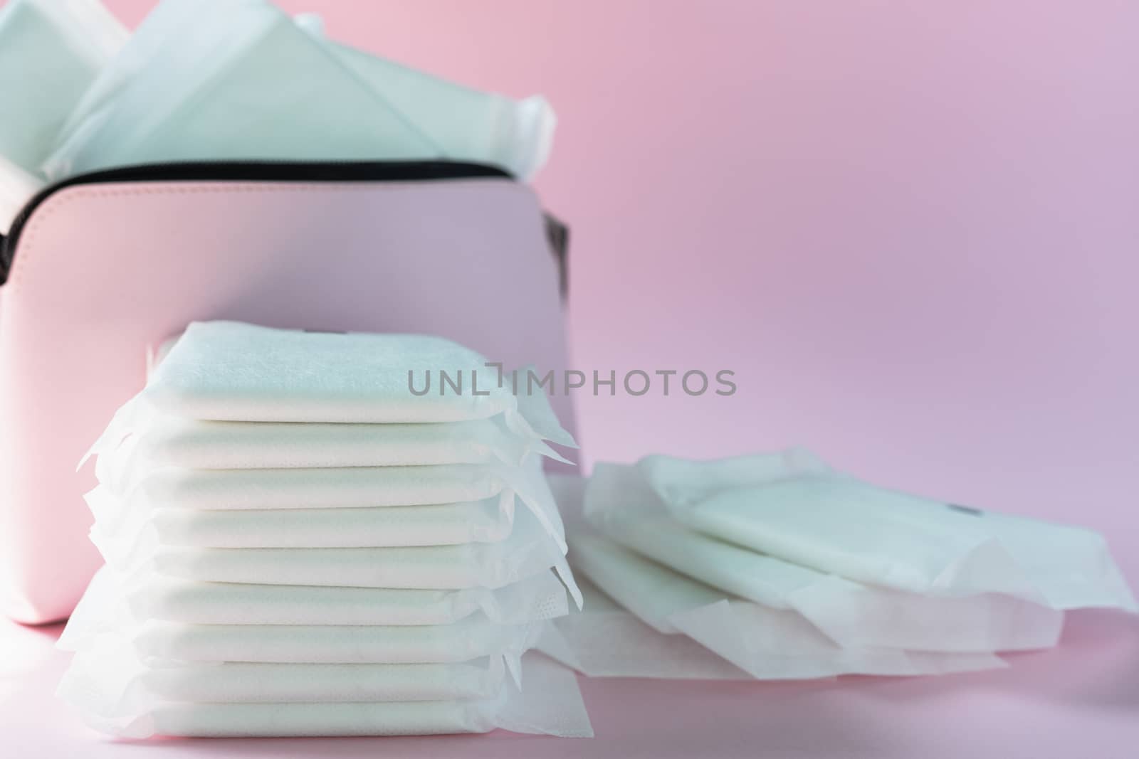 Feminine sanitary napkin, an absorbent item worn by a woman while menstruating, with blurred women's bag on pink background for hygiene and health concept