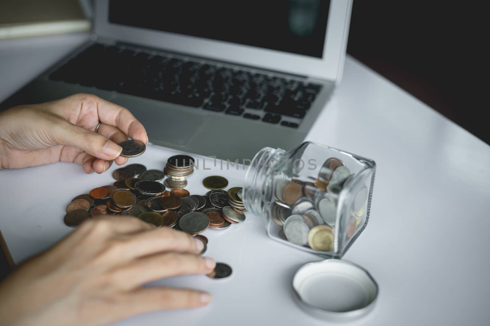 Woman's hand saving and counting money coins in the glass jar with computer laptop for planning, business and finance concept