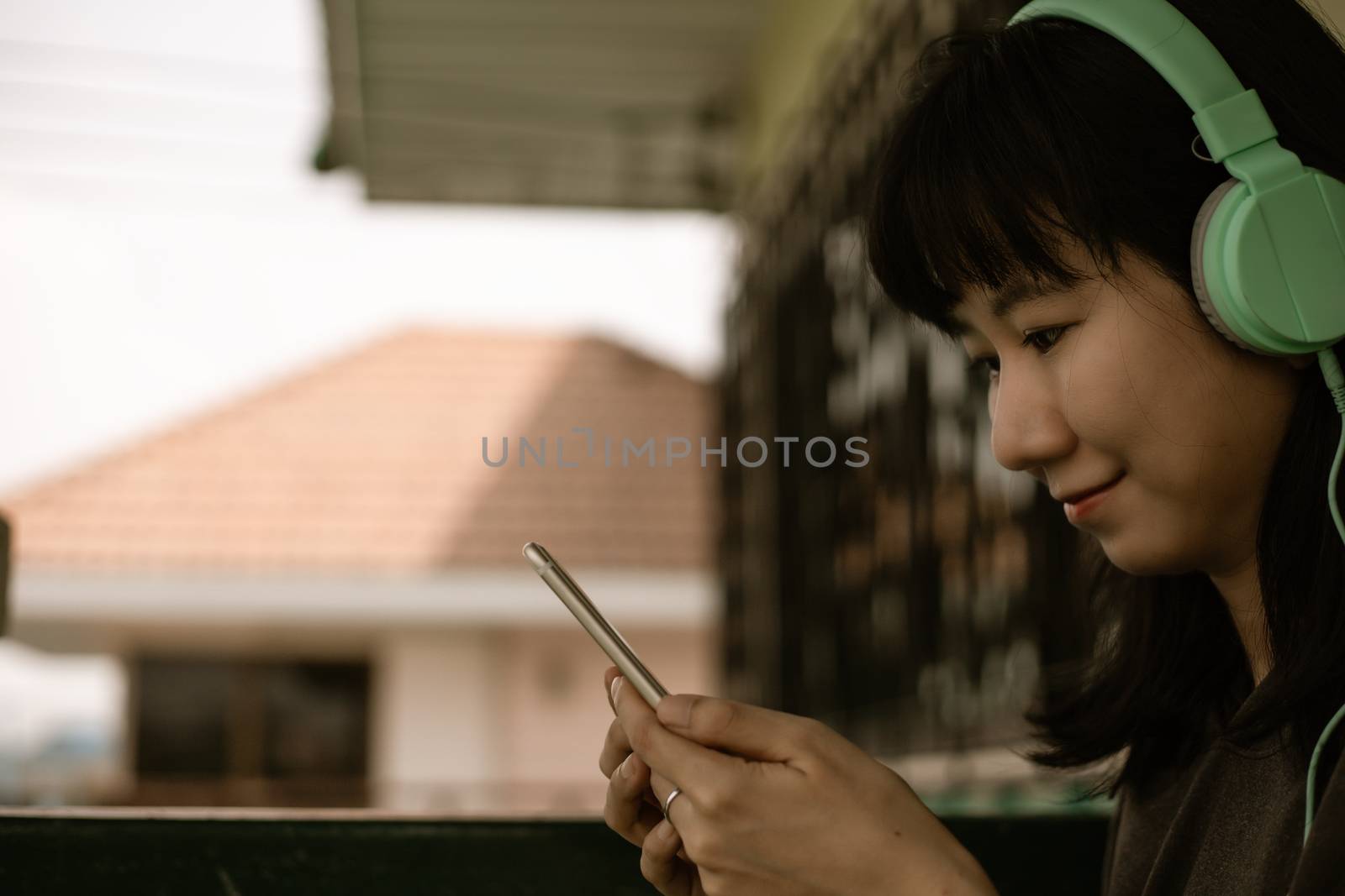 sian woman wearing headphones, using smartphone and staying home by iamnoonmai