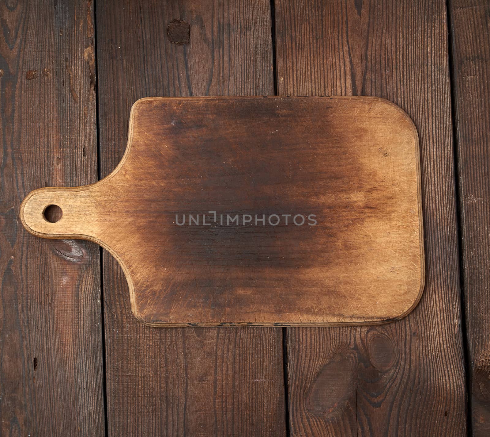 very old empty wooden rectangular cutting board, top view, brown wooden background 