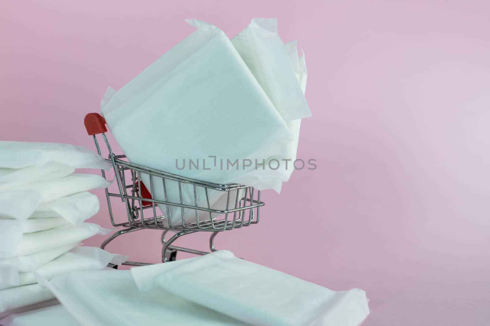 Feminine sanitary napkin, an absorbent item worn by a woman while menstruating, with shopping cart on pink background for hygiene and health concept