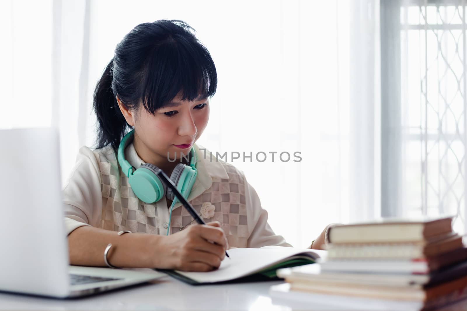 Asian woman writing on the paper, using laptop and working at home by iamnoonmai
