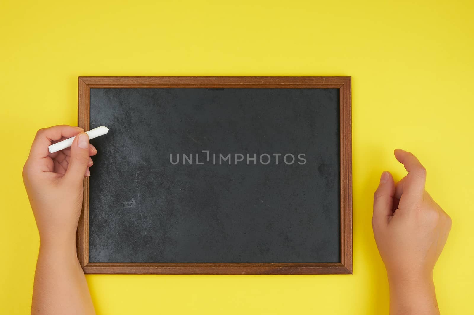 black chalk frame and two female hands with a piece of white chalk, yellow background 