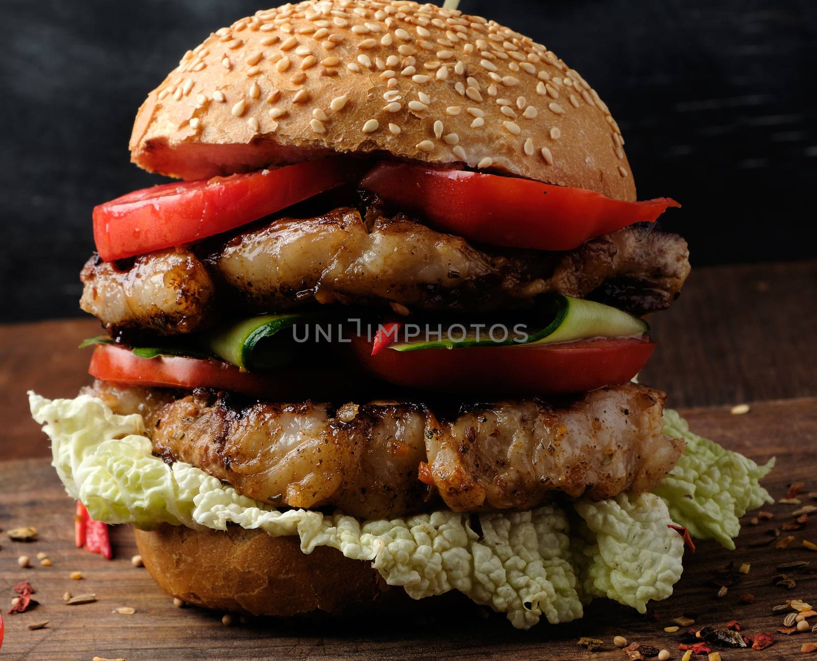 hamburger with pork fried steak, red tomatoes, fresh round bun with sesame seeds on a vintage brown wooden board