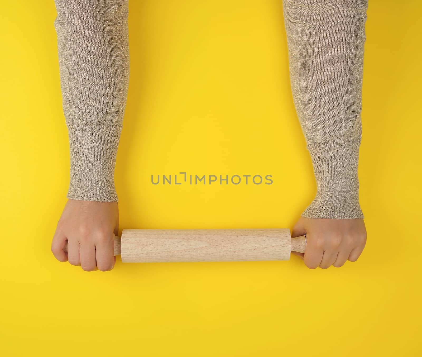 hand holding a wooden rolling pin on a yellow background, top view