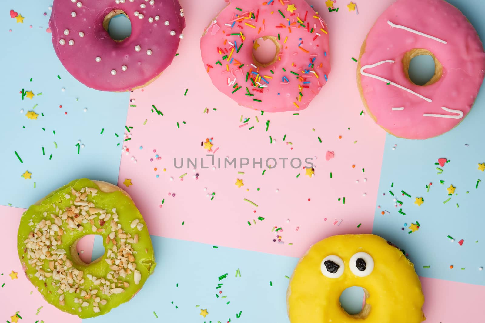 whole round pink donuts with colored sprinkles lie on a blue-pink background, top view, pastel colors