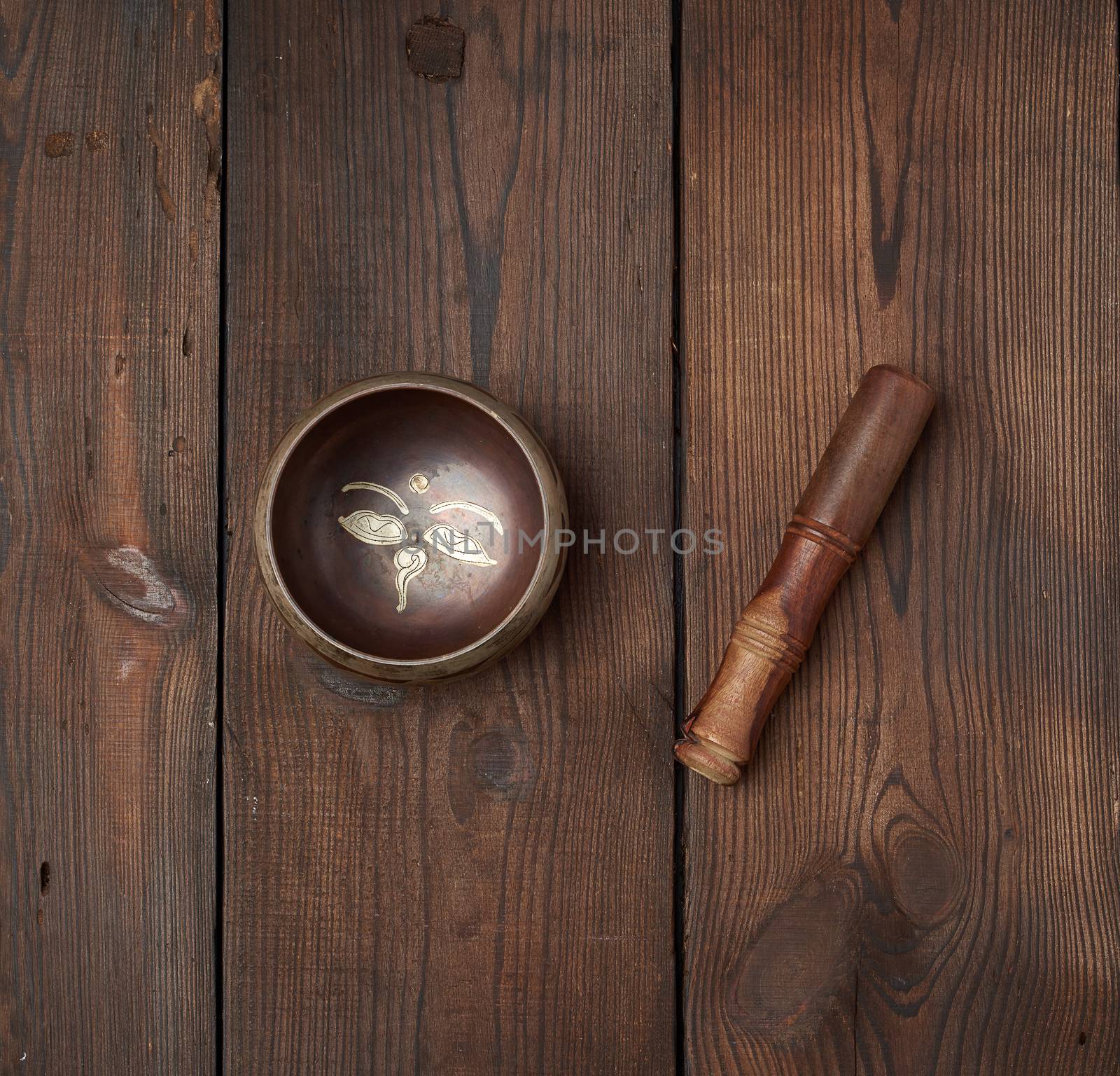 singing Tibetan copper bowl and wooden stick on a table of brown boards, top view
