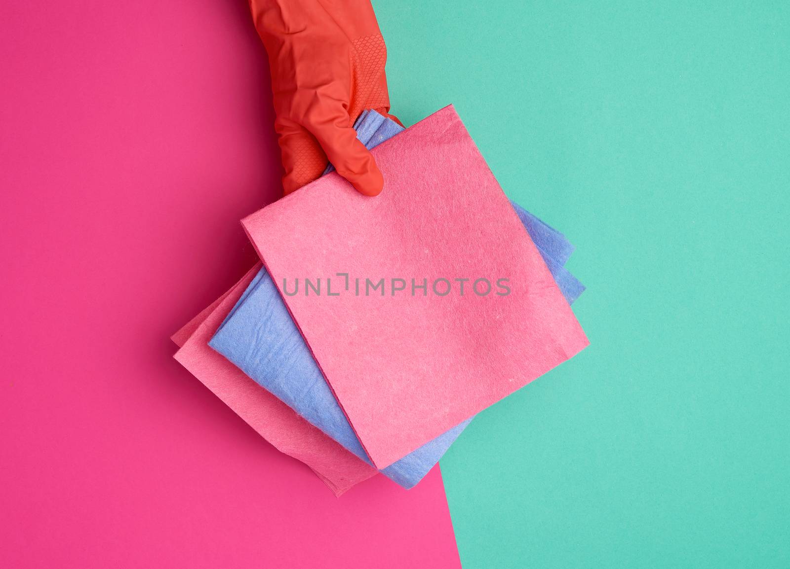  viscose rag for cleaning dust in the house in hands with an orange glove on, colored background