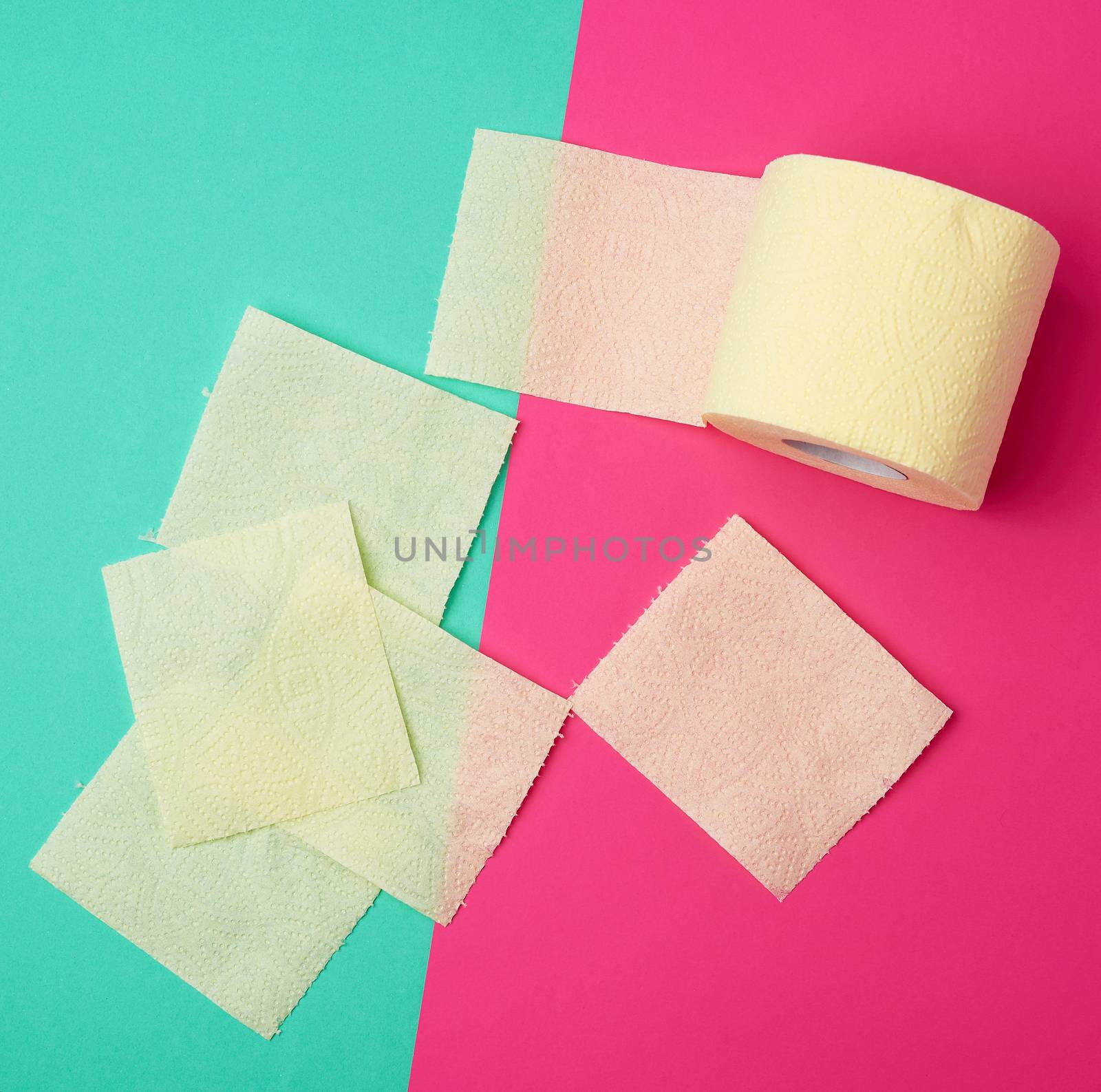 soft yellow toilet paper in a roll and torn pieces on a green-pink background, top view