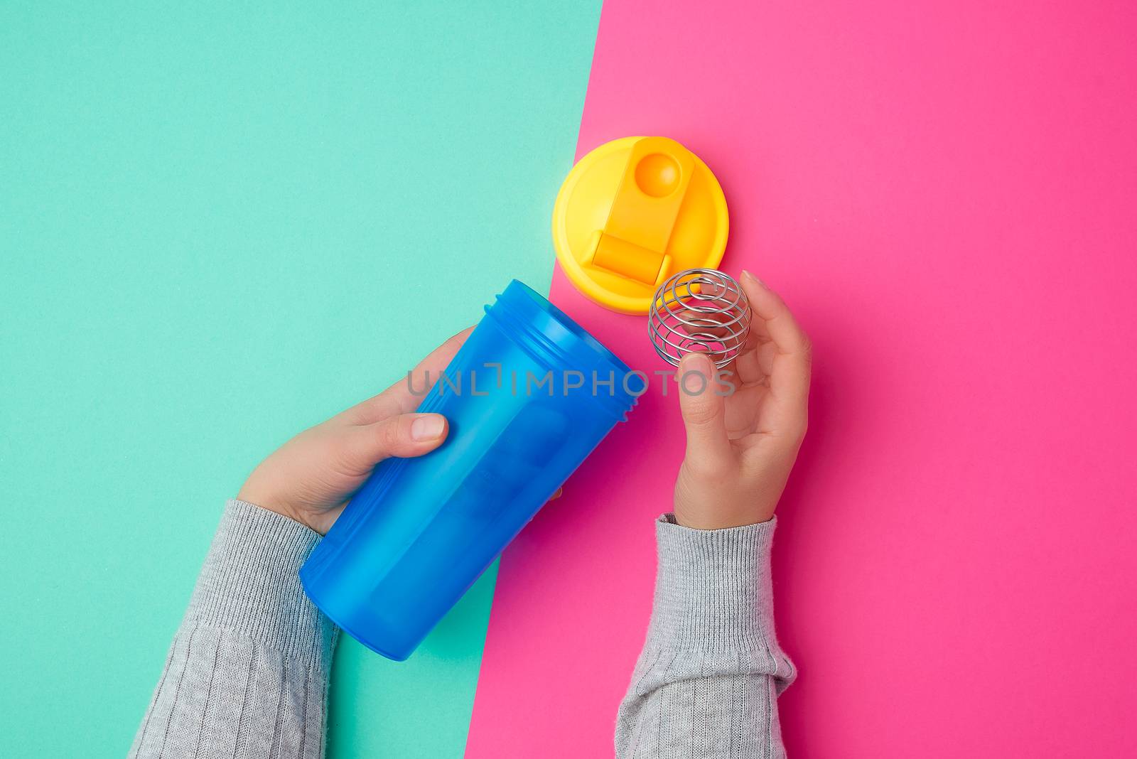 plastic blue shaker bottle with a yellow cap and an iron ball for sports people on a colored background, top view