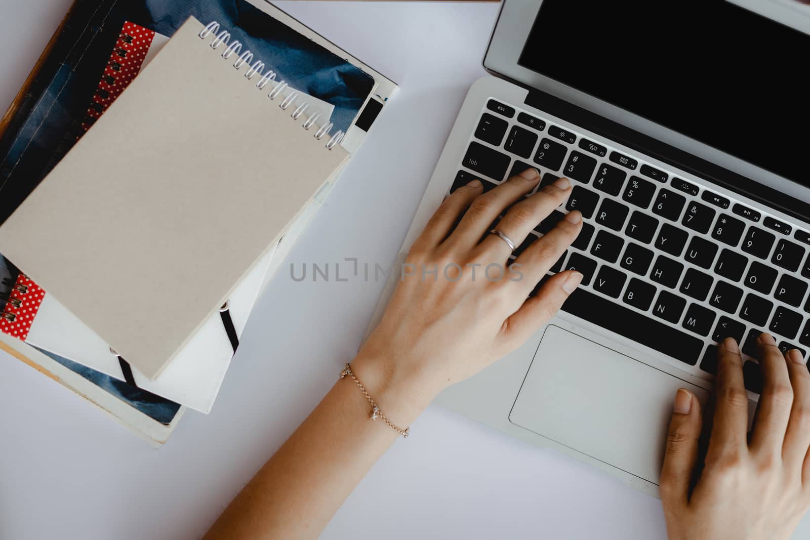 Top view of hand using computer laptop with a stack of books on white office desk for e-learning, work at home and workspace concept