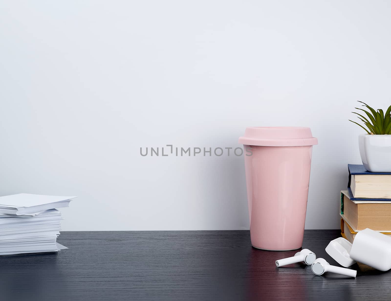 wireless white headphones with charging, pink ceramic cup with coffee and white sheets for notes on a black table, workplace
