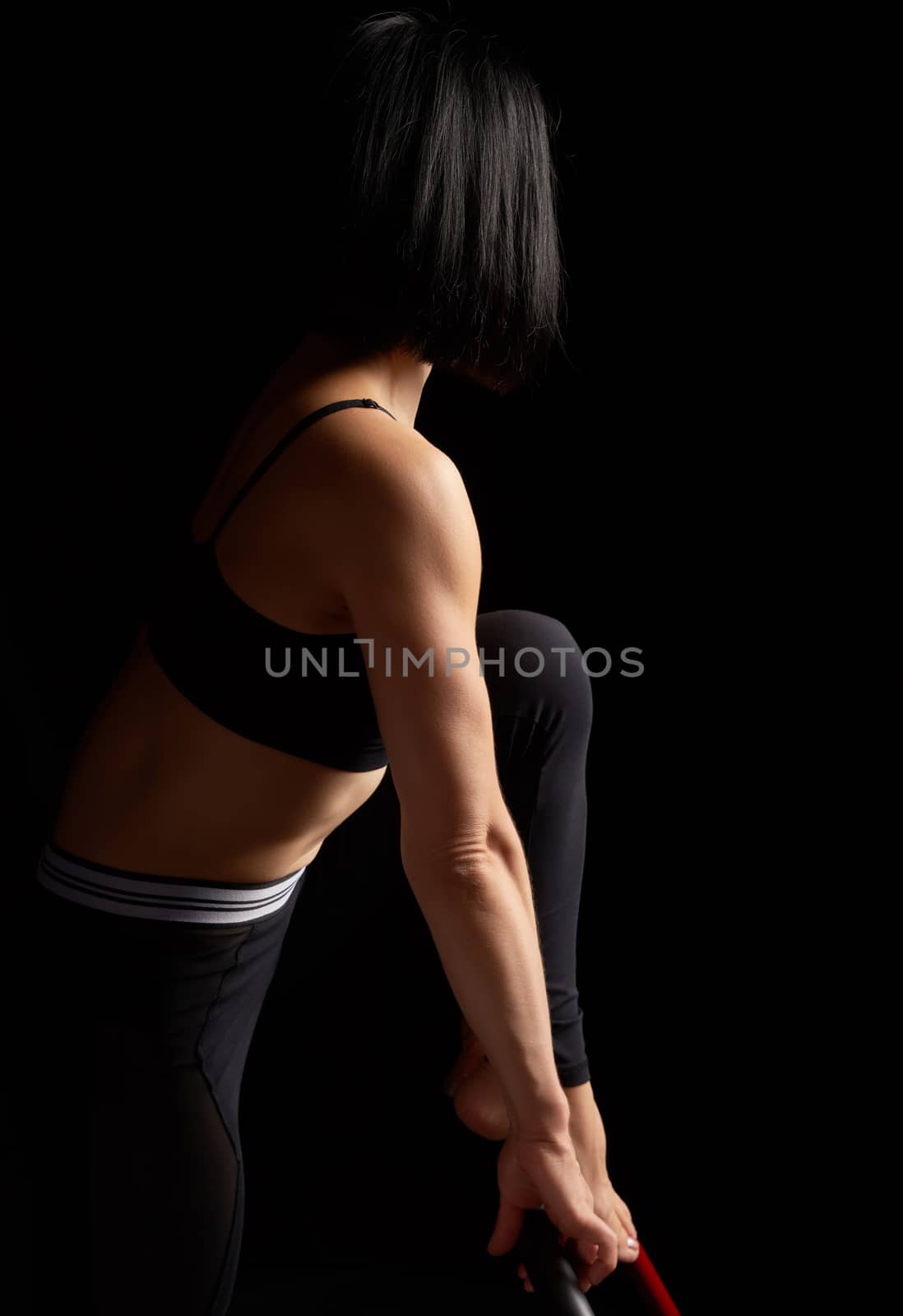girl with a sports figure short black hair does sports exercises on the simulator, dark background, athlete stands sideways
