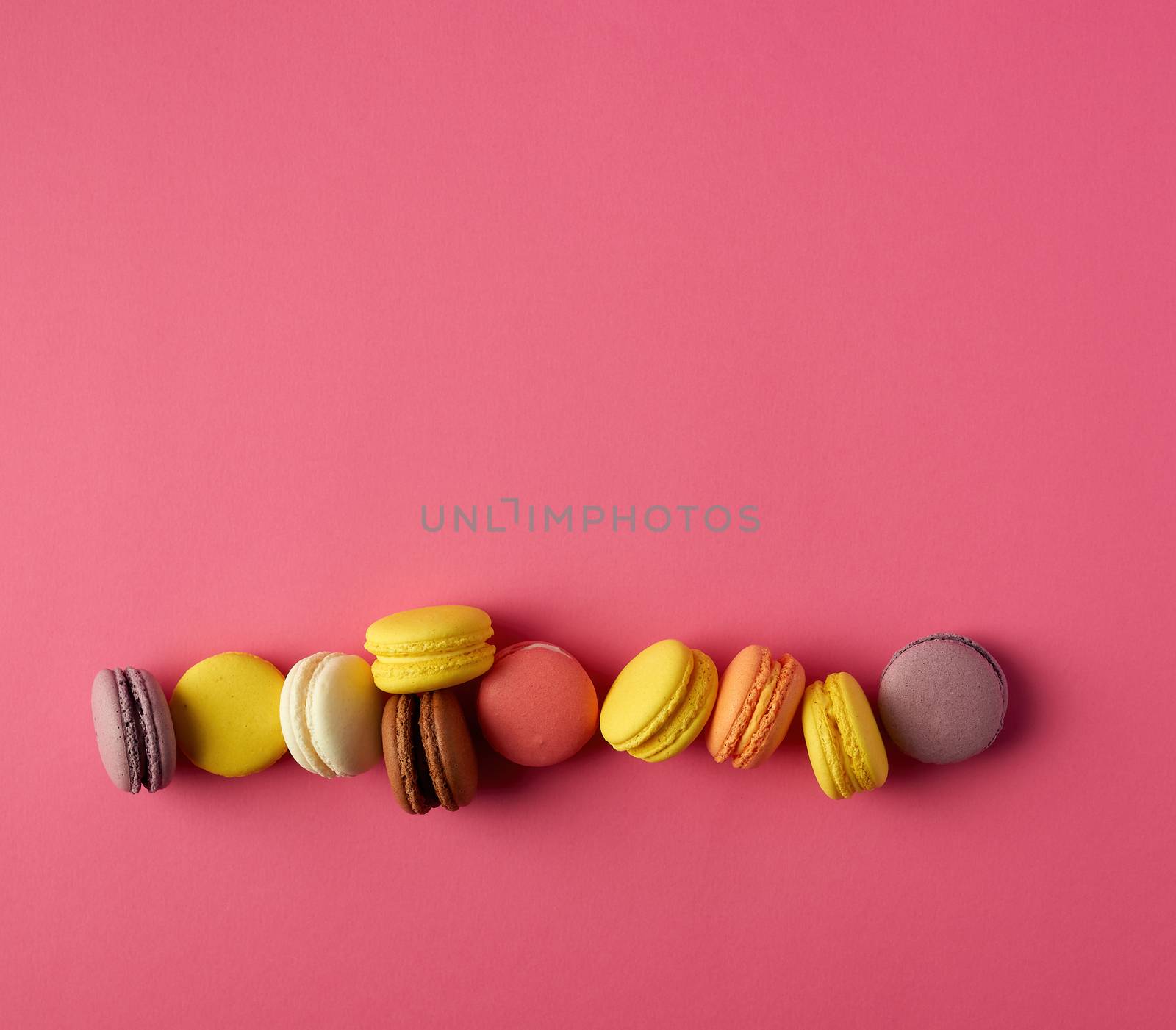 round multi-colored baked macarons with cream lie in a line on a red background, flat lay, copy space 