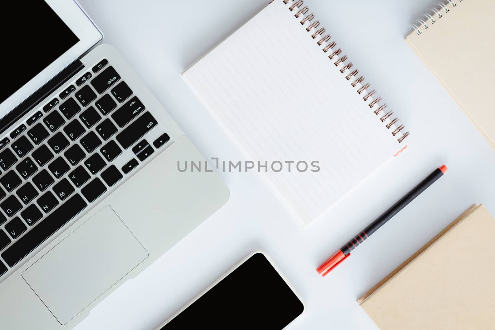 Top view of white office desk with laptop computer, smartphone, notebook and a pen for business and workspace concept