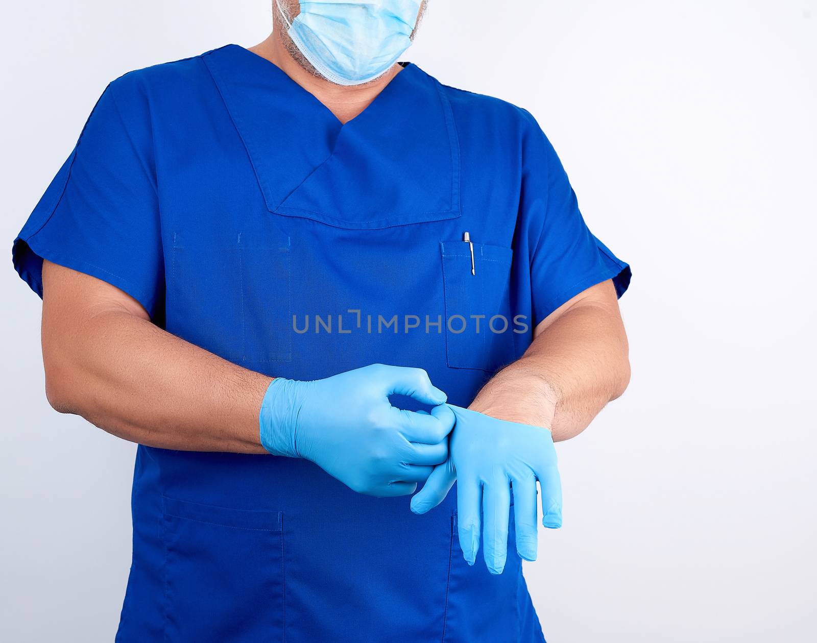 male doctor in blue uniform puts on his hands blue sterile latex gloves before surgery, white background