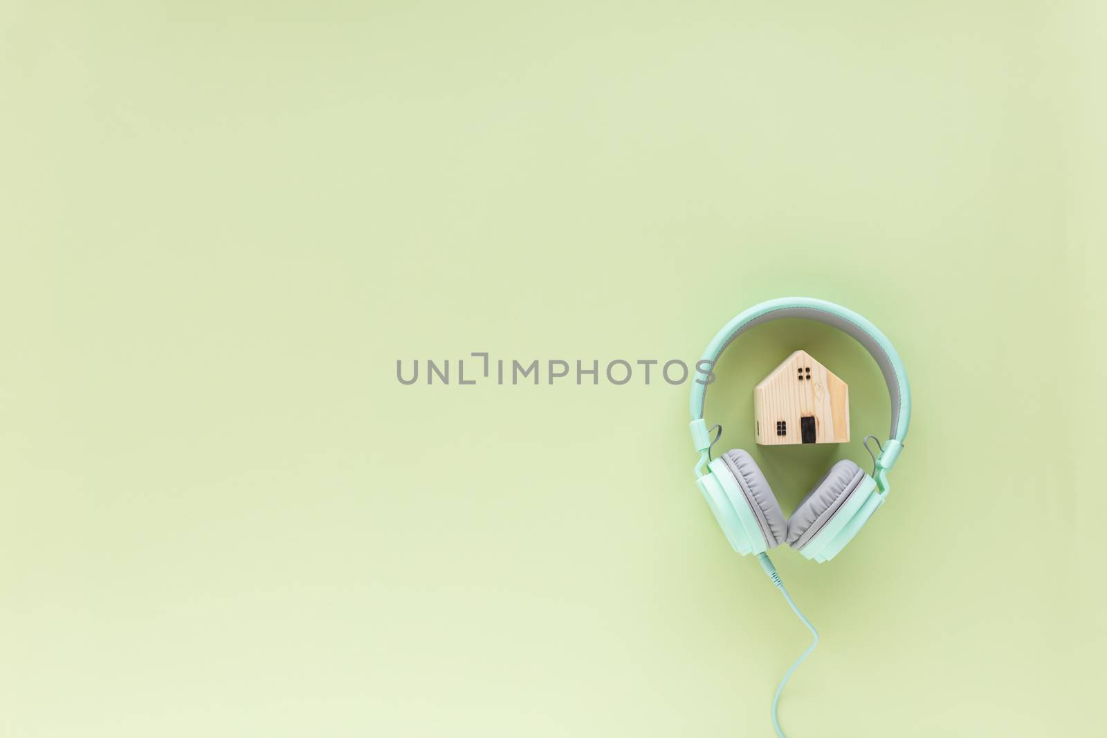 Green headphones with wooden house model on green background with copy space for time to relax,  self-quarantine, staying home and social distancing in coronavirus or Covid-19 outbreak situation