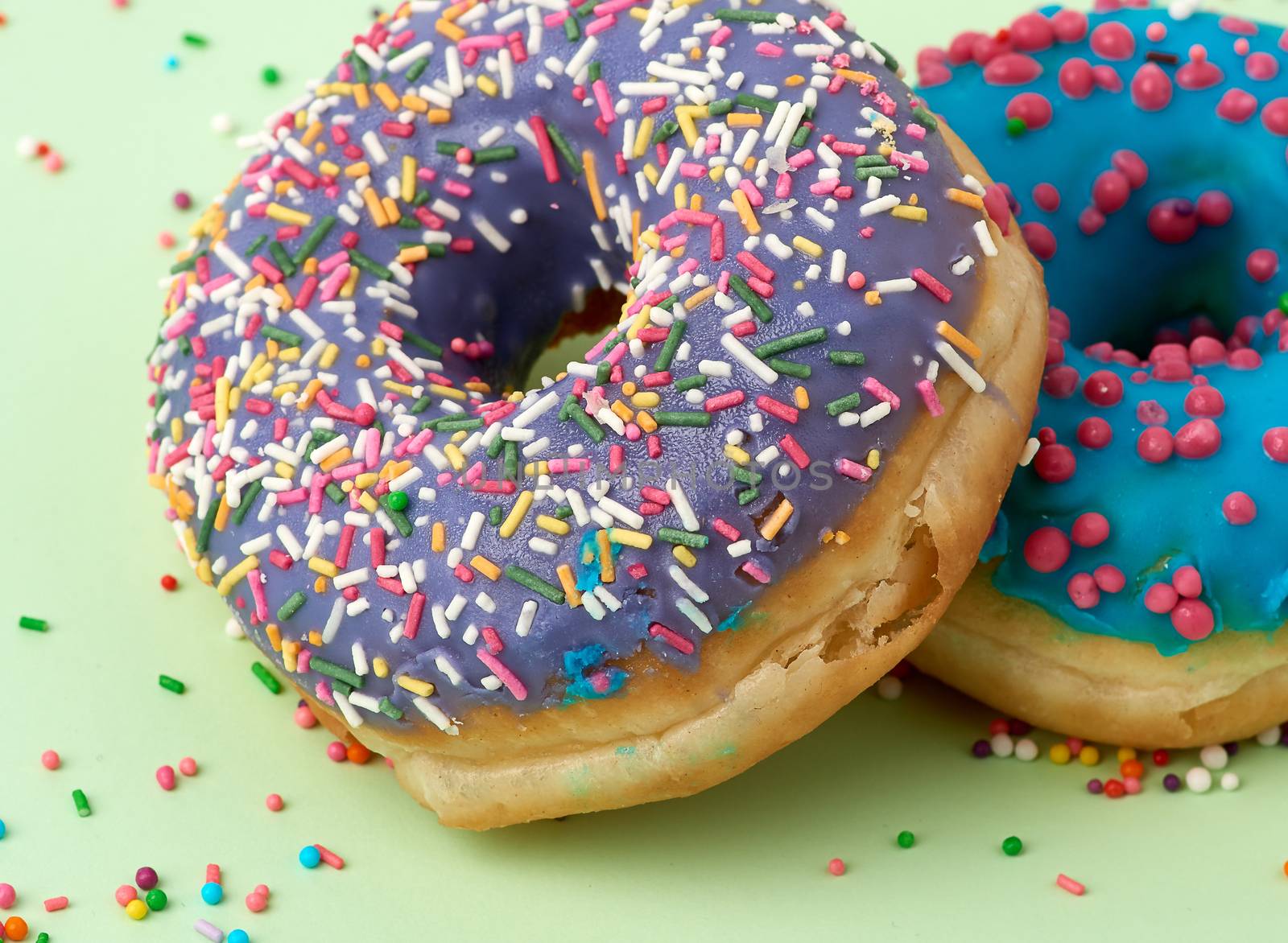 round baked donut with colored sugar sprinkles and with blue sugar icing on a green background, close up