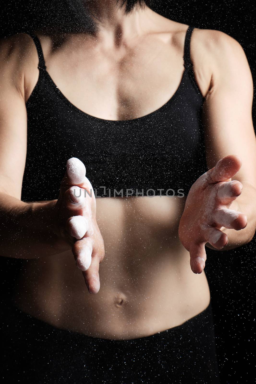 young girl with a sports figure dressed in a black top claps in her hands with white magnesia, preparing before exercise, low key