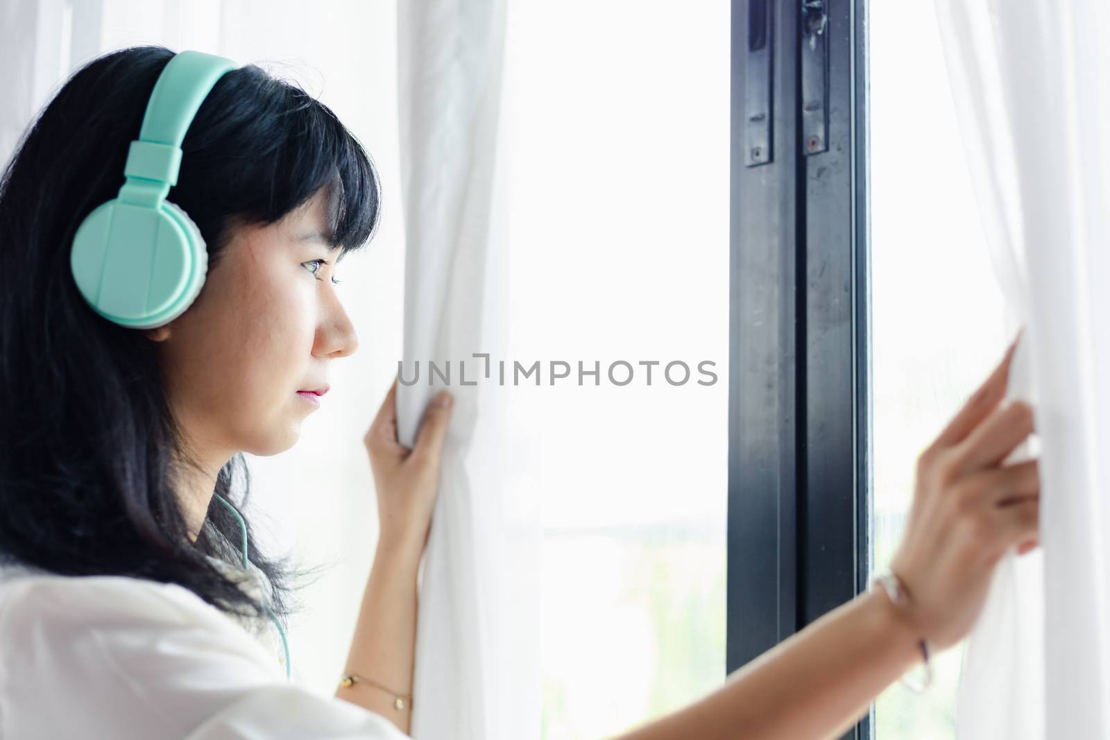 Asian woman staying home, wearing headphones and standing absent-minded at the door by iamnoonmai