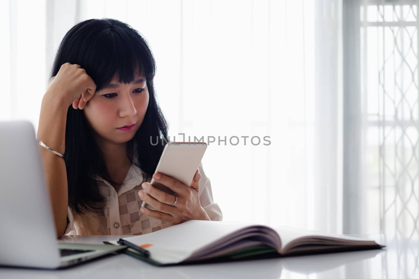 Asian woman using smartphone with computer laptop and working at home for business, self-quarantine, staying home and social distancing in coronavirus or Covid-2019 outbreak situation concept