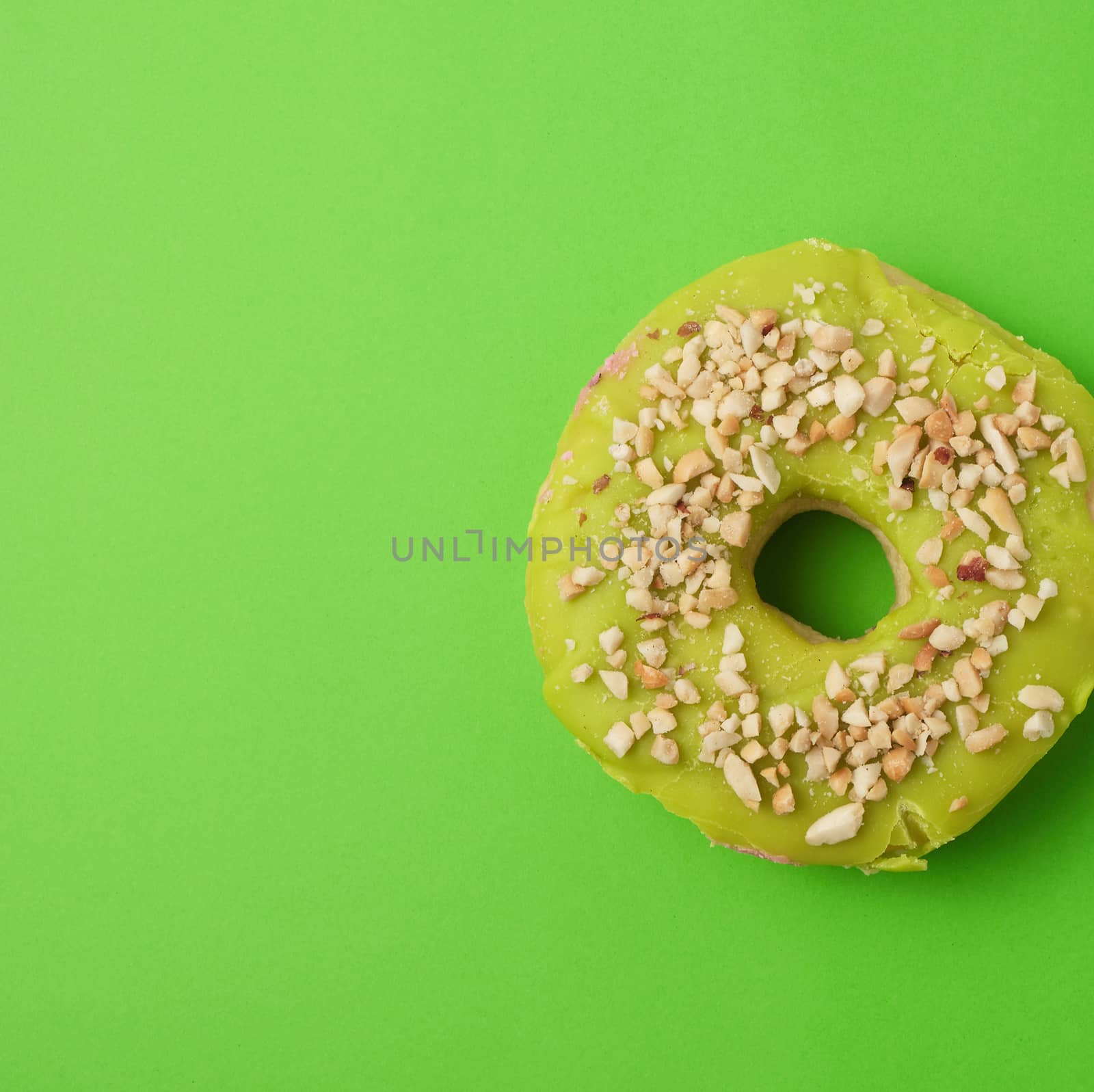round baked donut with green pistachio glaze sprinkled with crushed nuts, green background, feed on top