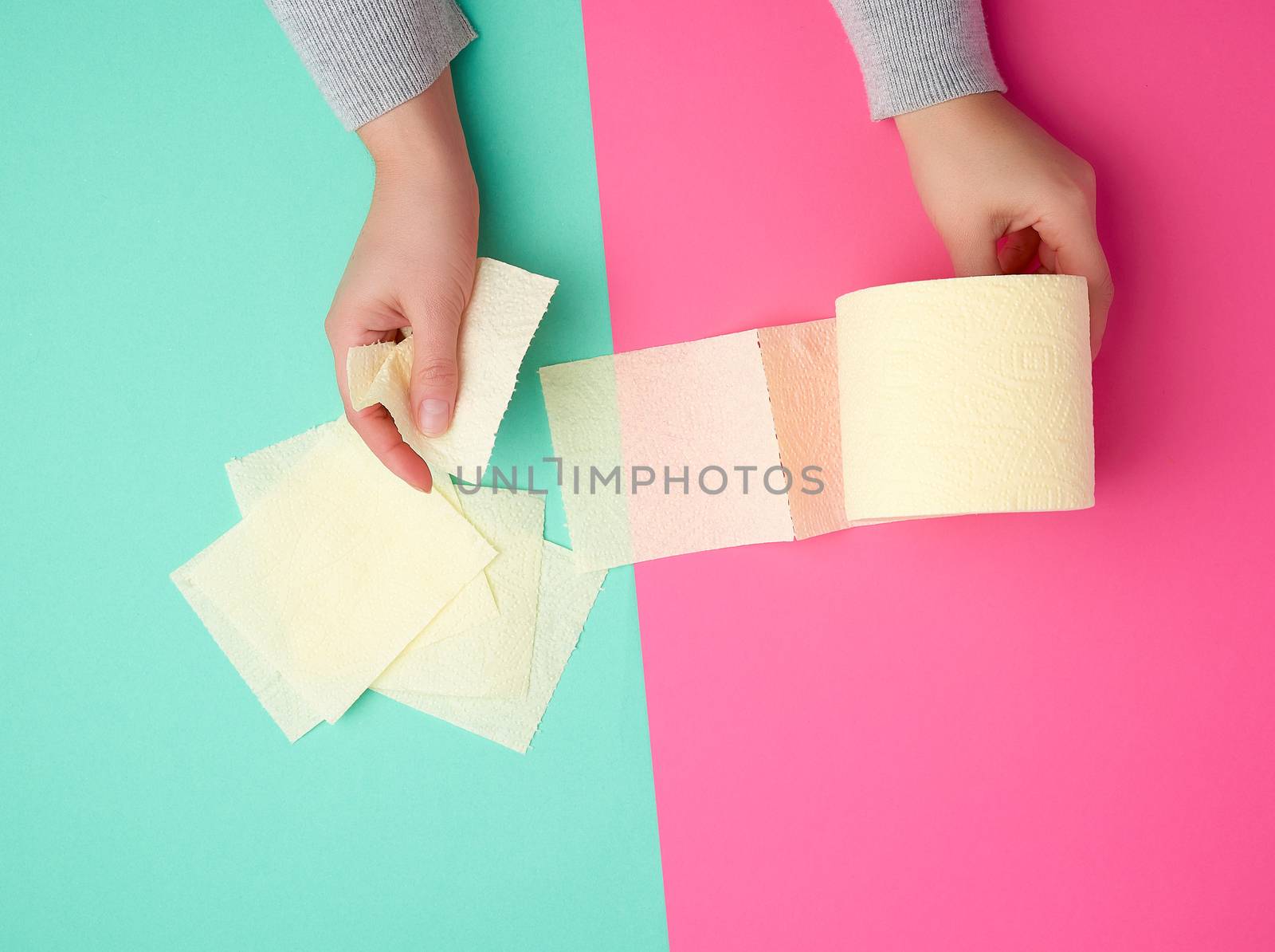 roll of yellow toilet paper in female hands, torn pieces on a colored background, top view