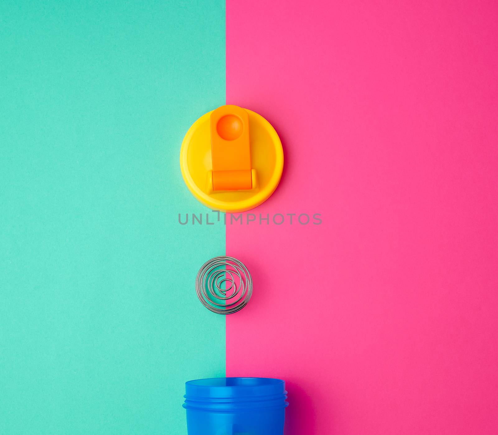 plastic blue shaker bottle with a yellow cap and an iron ball for sports people on a colored background, top view