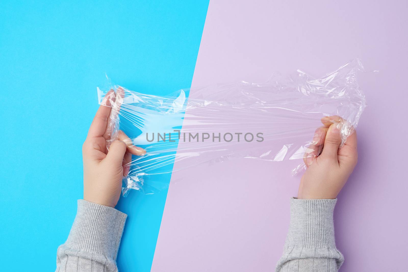 two hands hold a piece of transparent plastic film on a colored background, top view