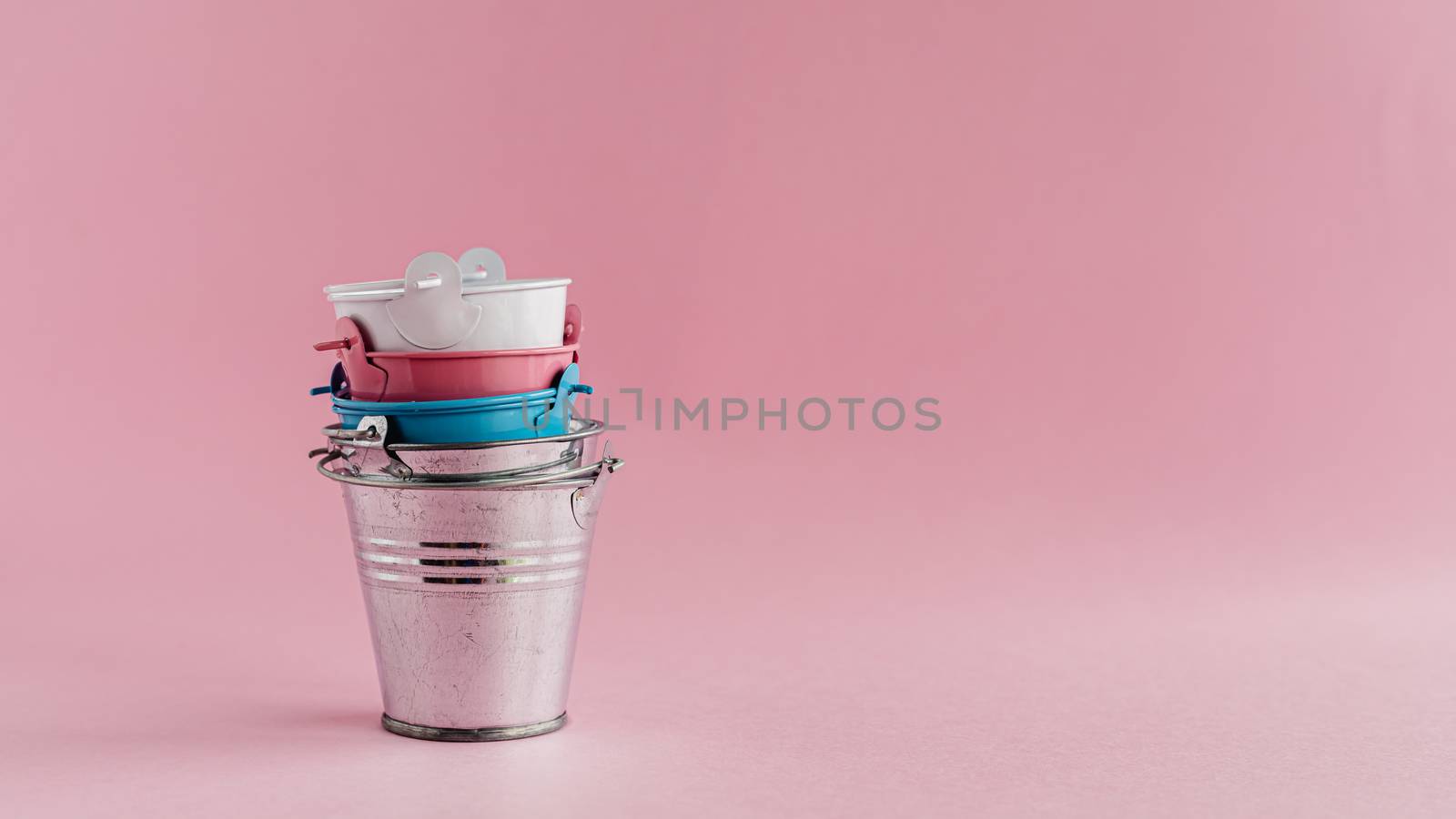 Mini colored tin pails or buckets on pink background with copy space for household items concept