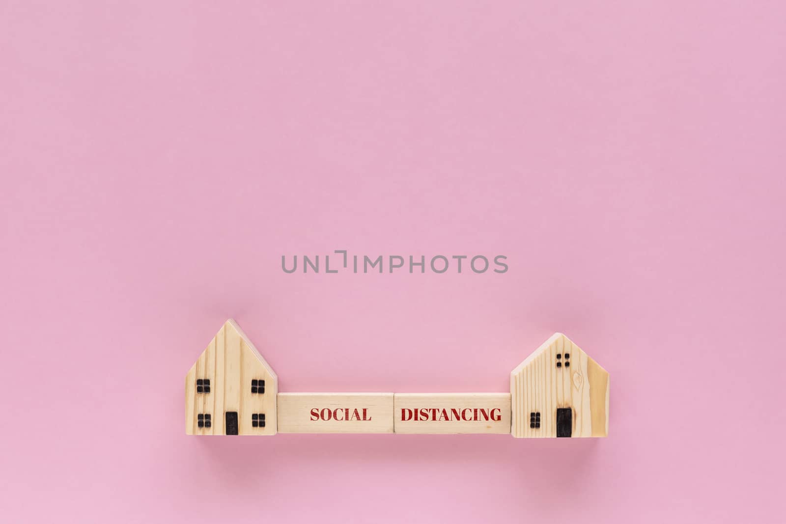 Wooden house model with social distancing text on pink background for self-quarantine and staying home in coronavirus or Covid-19 situation concept