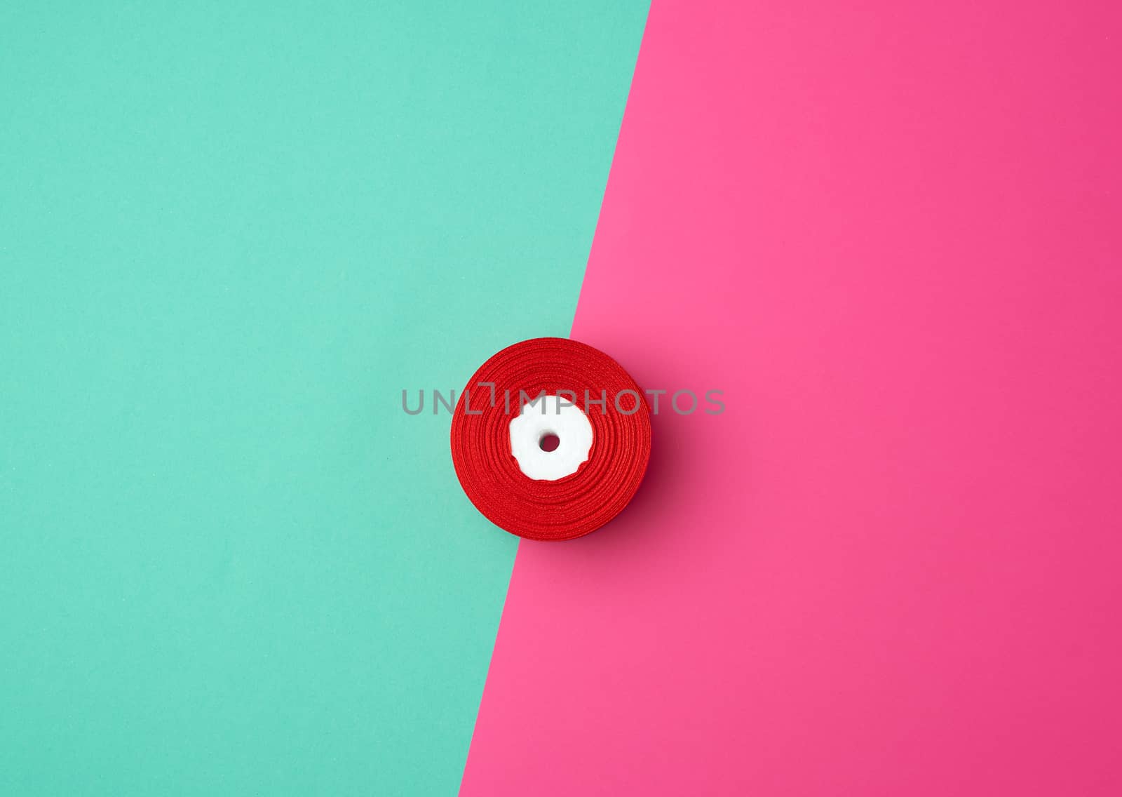 spools with red satin ribbon on a green pink background, top view