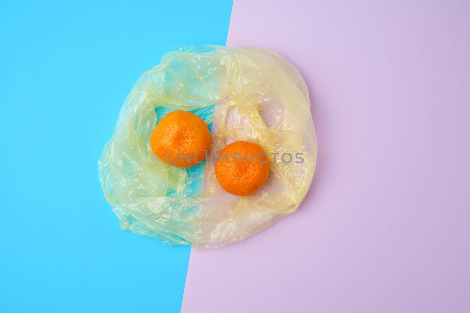 two ripe orange mandarins lie in a transparent plastic bag on a color background, top view
