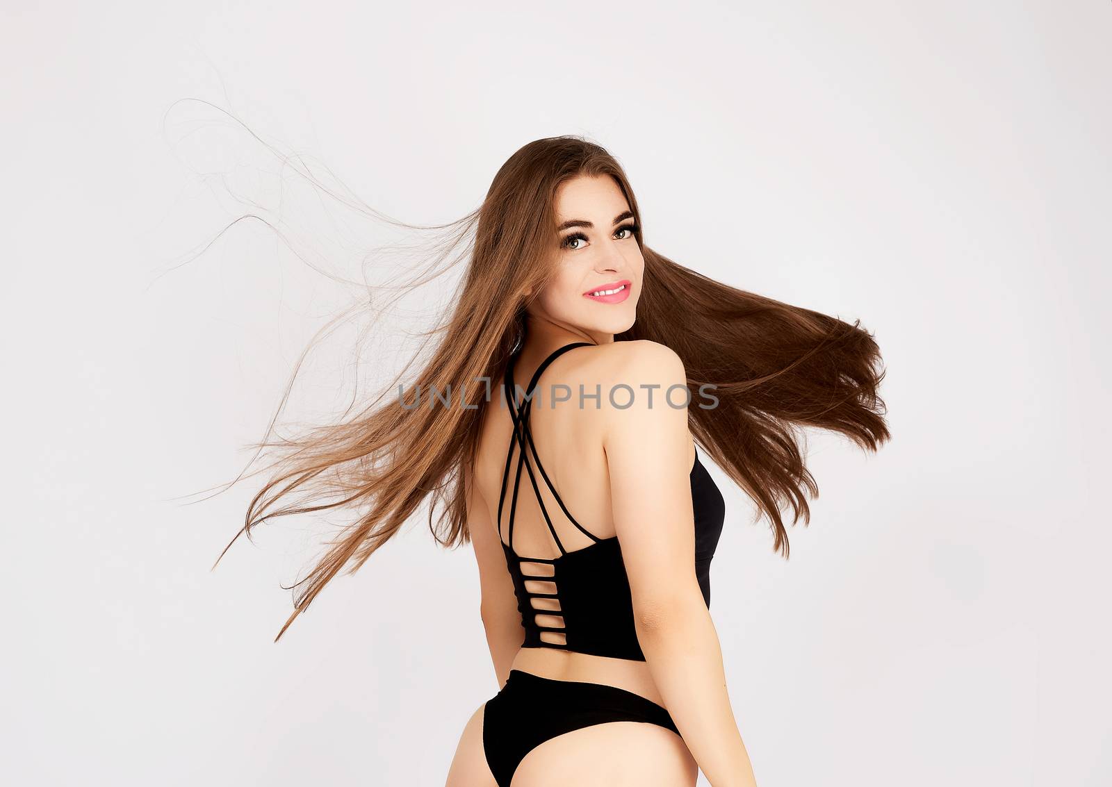 girl with long blond hair smiles at the camera on a white background, sporty fit figure, dressed in a black sconce and bikini, hair fluttering in the wind