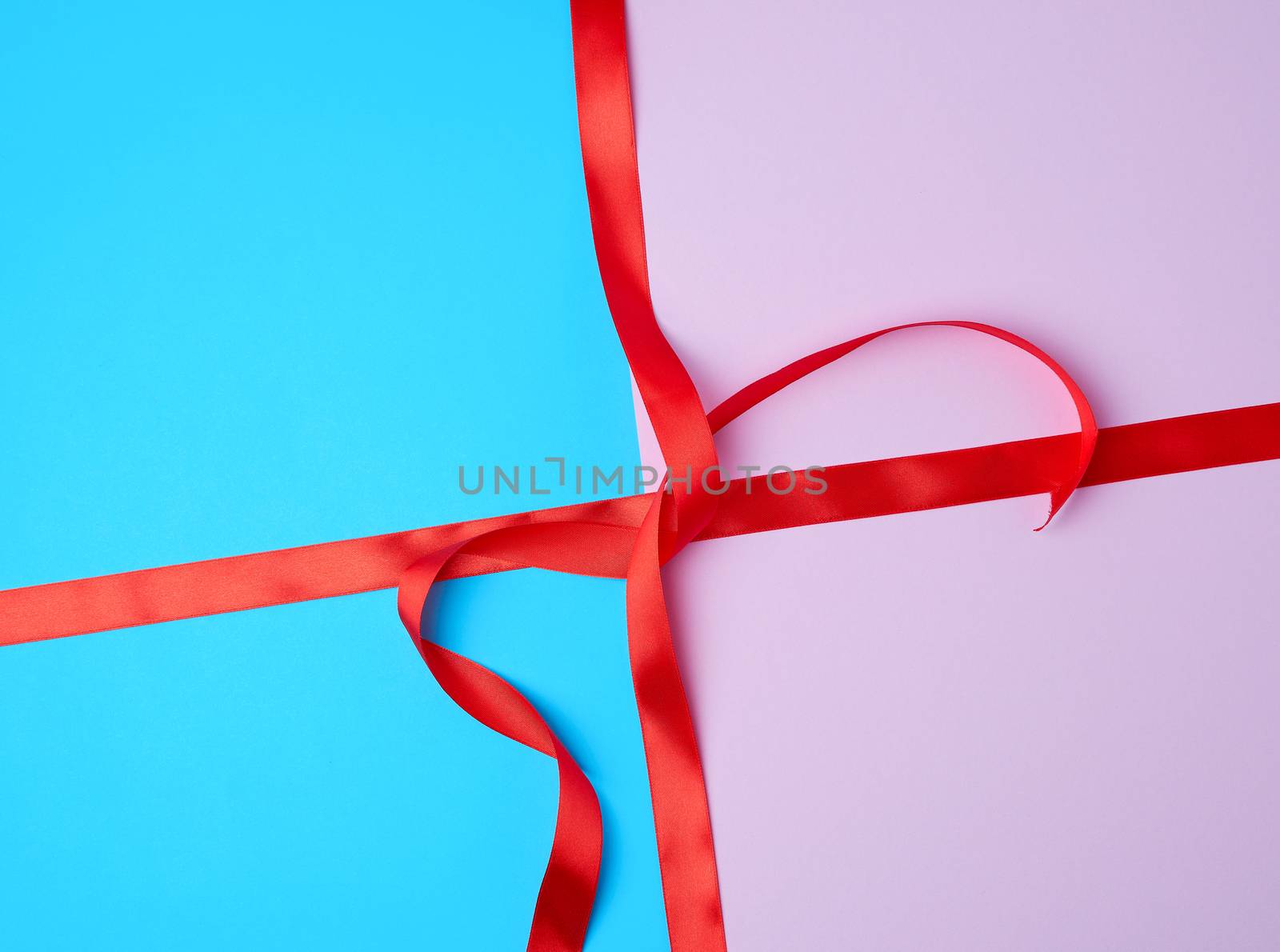 red satin ribbon on a colored background, imitation of tying and packing a gift