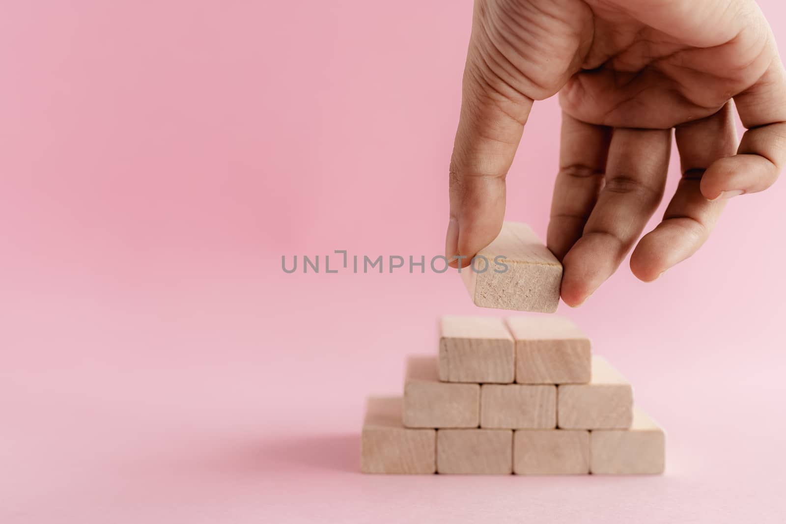 Hand putting the wooden toy on pink background for leisure activities concept