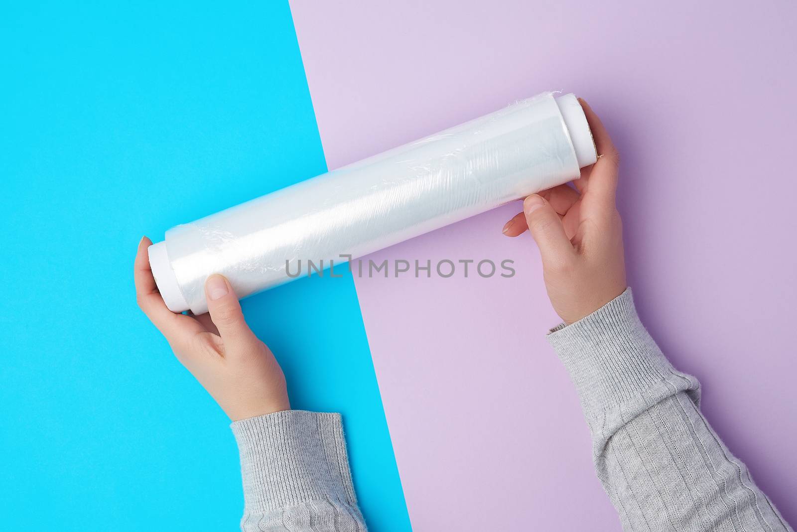 two hands hold a large roll of wound white transparent film for wrapping food, top view
