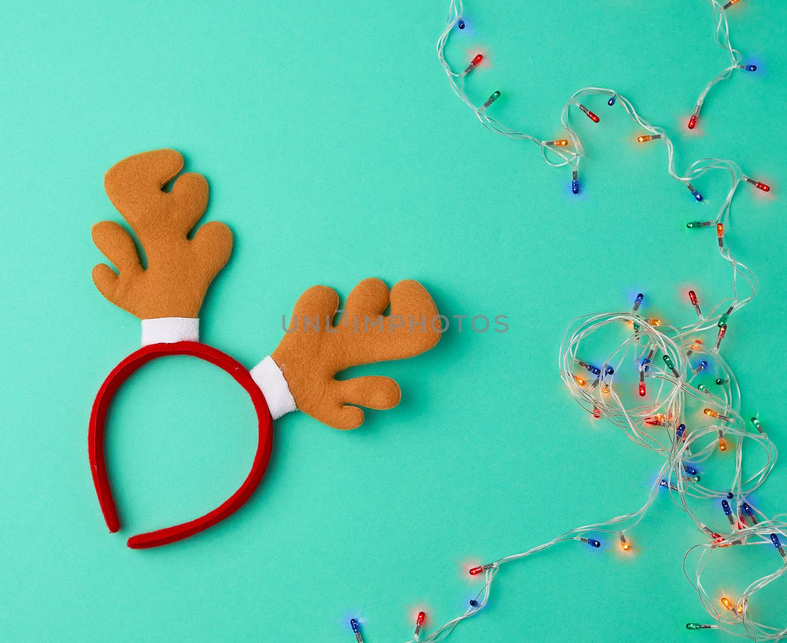 burning christmas garland on a white wire with colorful lights and carnival deer head mask on a green background