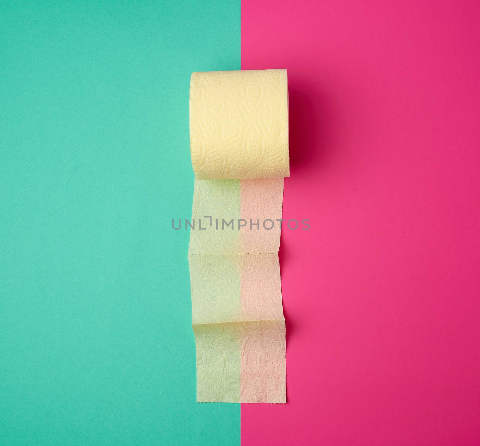 soft yellow toilet paper in a roll on a green-pink background, top view