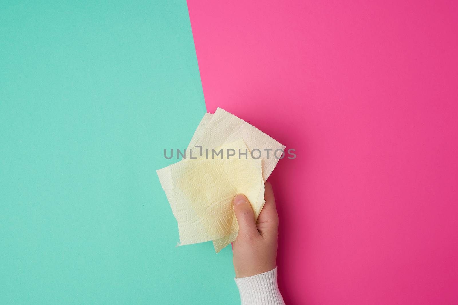 yellow toilet paper in female hands, torn pieces on a colored background, top view