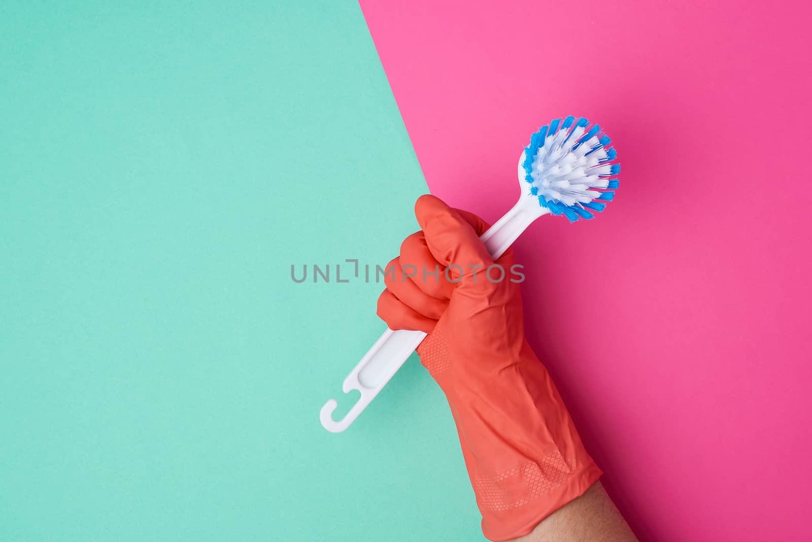 white plastic cleaning brush in hand, protective orange glove on hand, color background