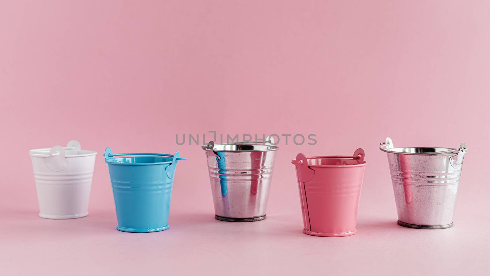 Mini colored tin pails or buckets on pink background with copy space for household items concept