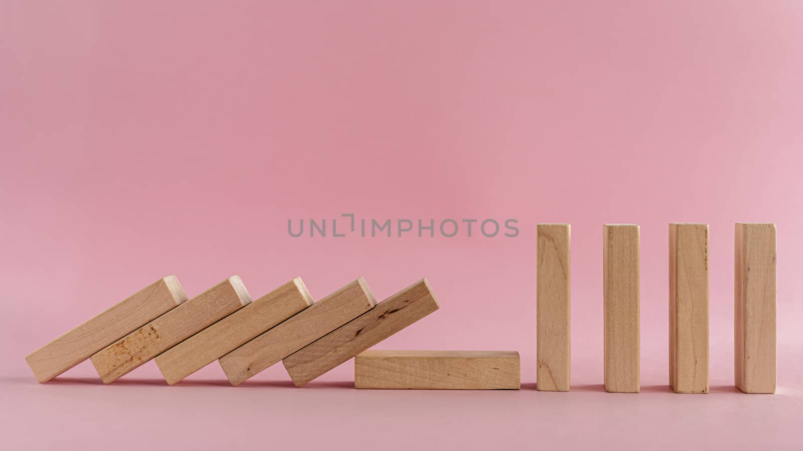 The wooden toys falling down but the next others that is far away could stand on pink background for social distancing concept